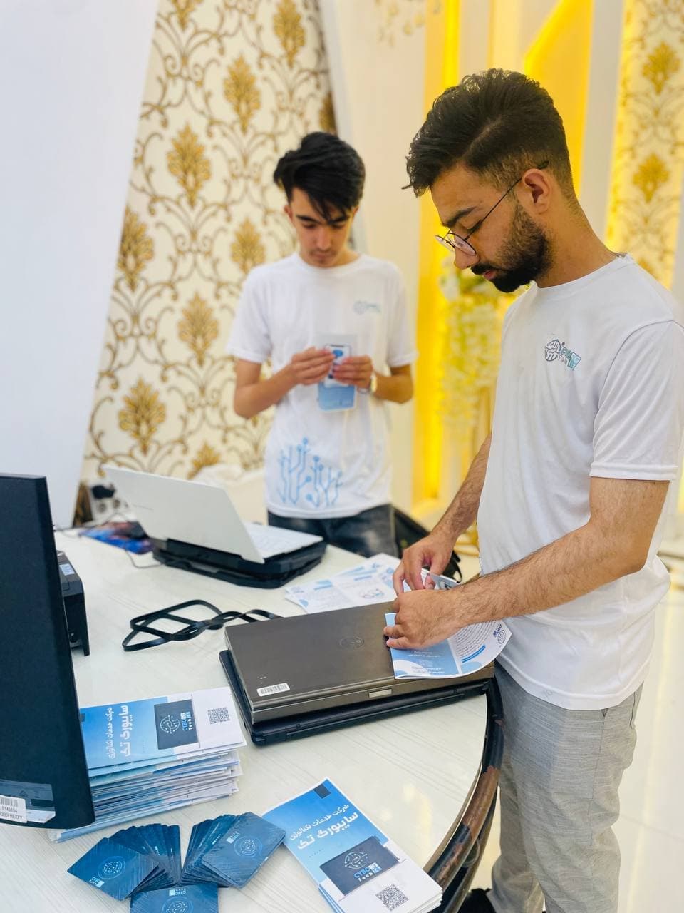Team members arranging brochures and laptops on the Cyborg Tech booth table